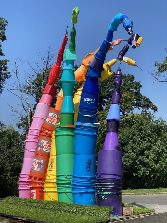 A photo of a rainbow sculpture made of plastic paint buckets.