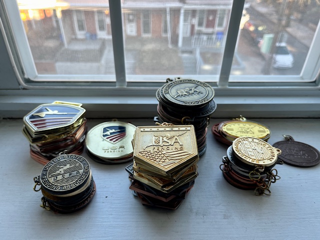 A bunch of national fencing medals piled up on a windowsill. Some are pentagons, some are disks.
